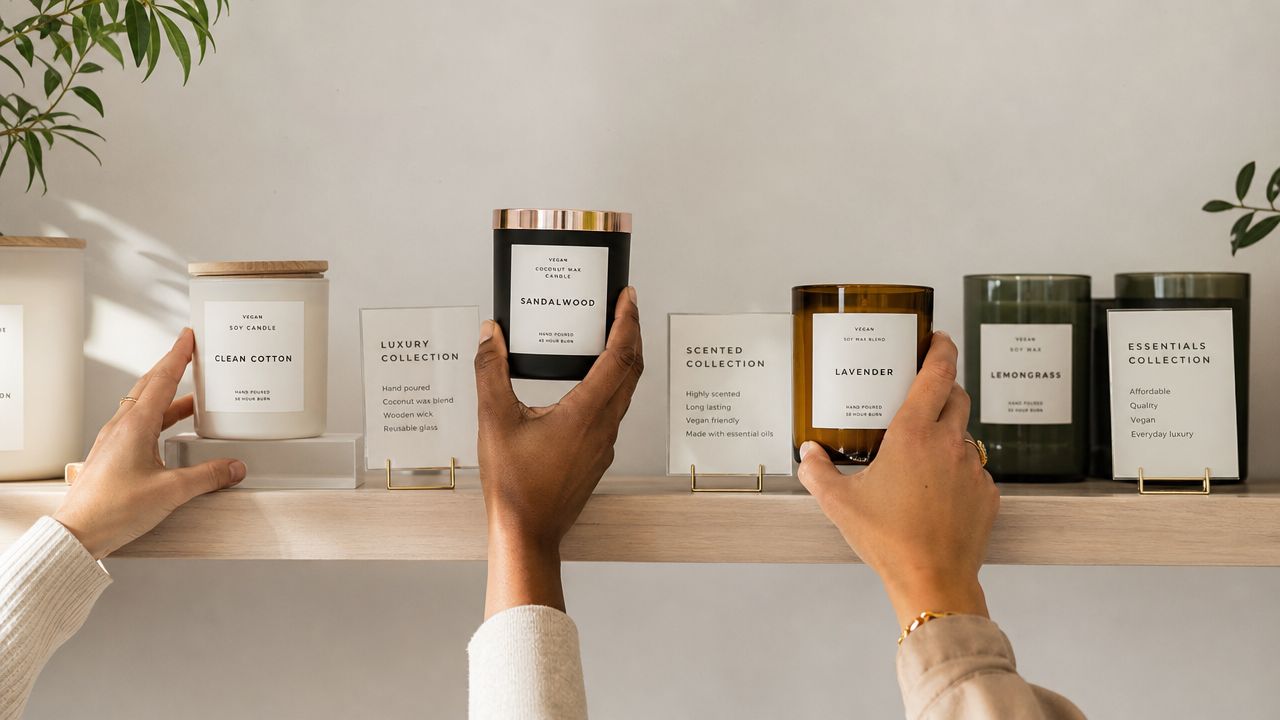 Two people selecting vegan candles from a store shelf featuring various scented collections and glass jars.