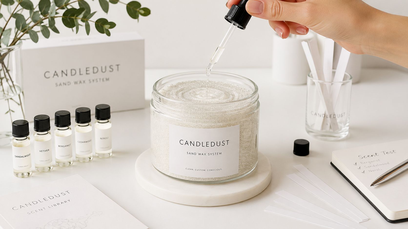 A hand using a dropper to add fragrance oil to a clear jar of Candledust sand wax.